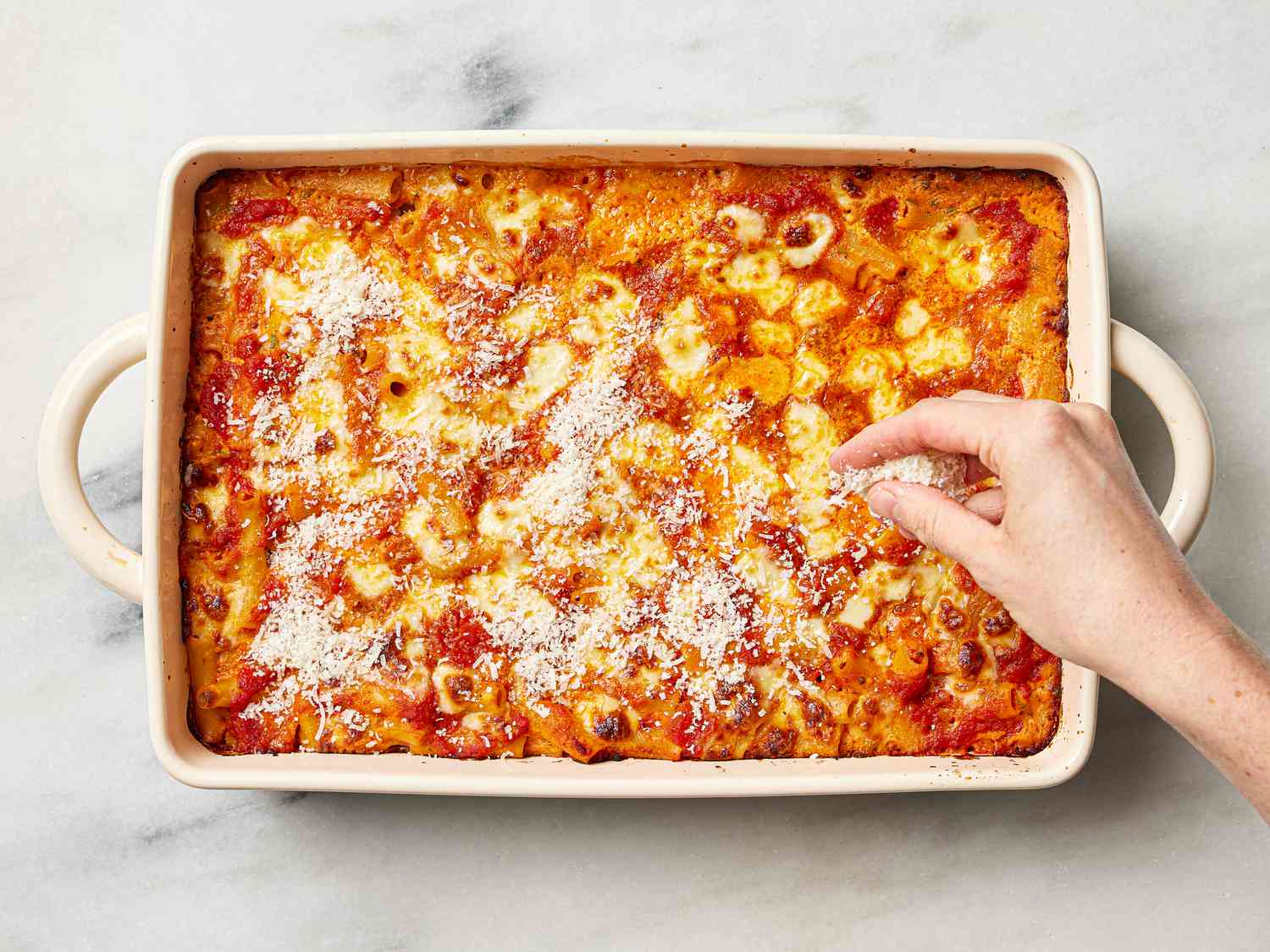 Overhead view of sprinkling cheese on baked ziti