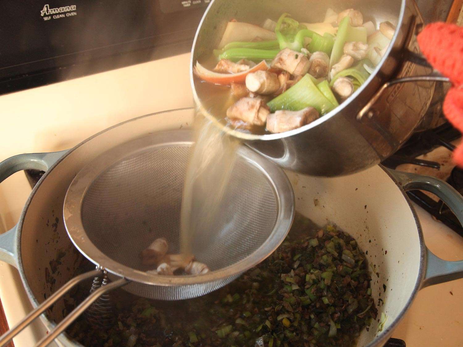 Vegetable stock being strained through a fine mesh strainer into a Dutch oven.
