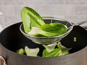 A metal spider strainer lifting bok chou from a stockpot