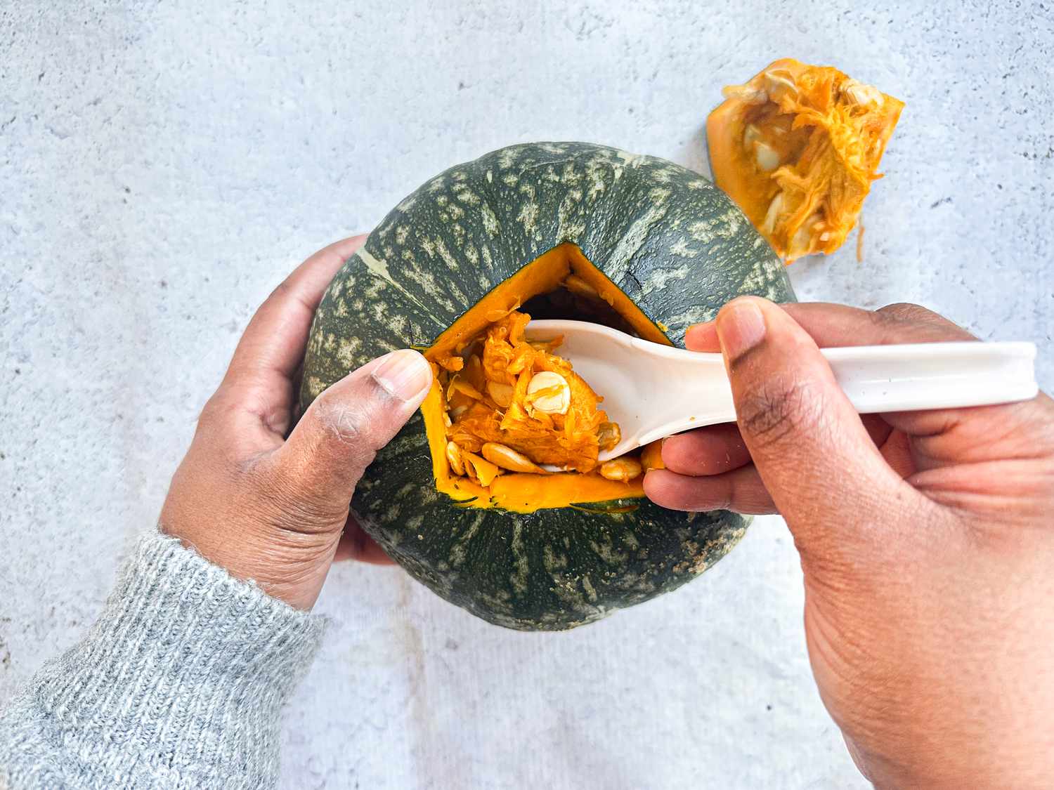 Hands scooping the filling of a pumpkin out of it on a white surface