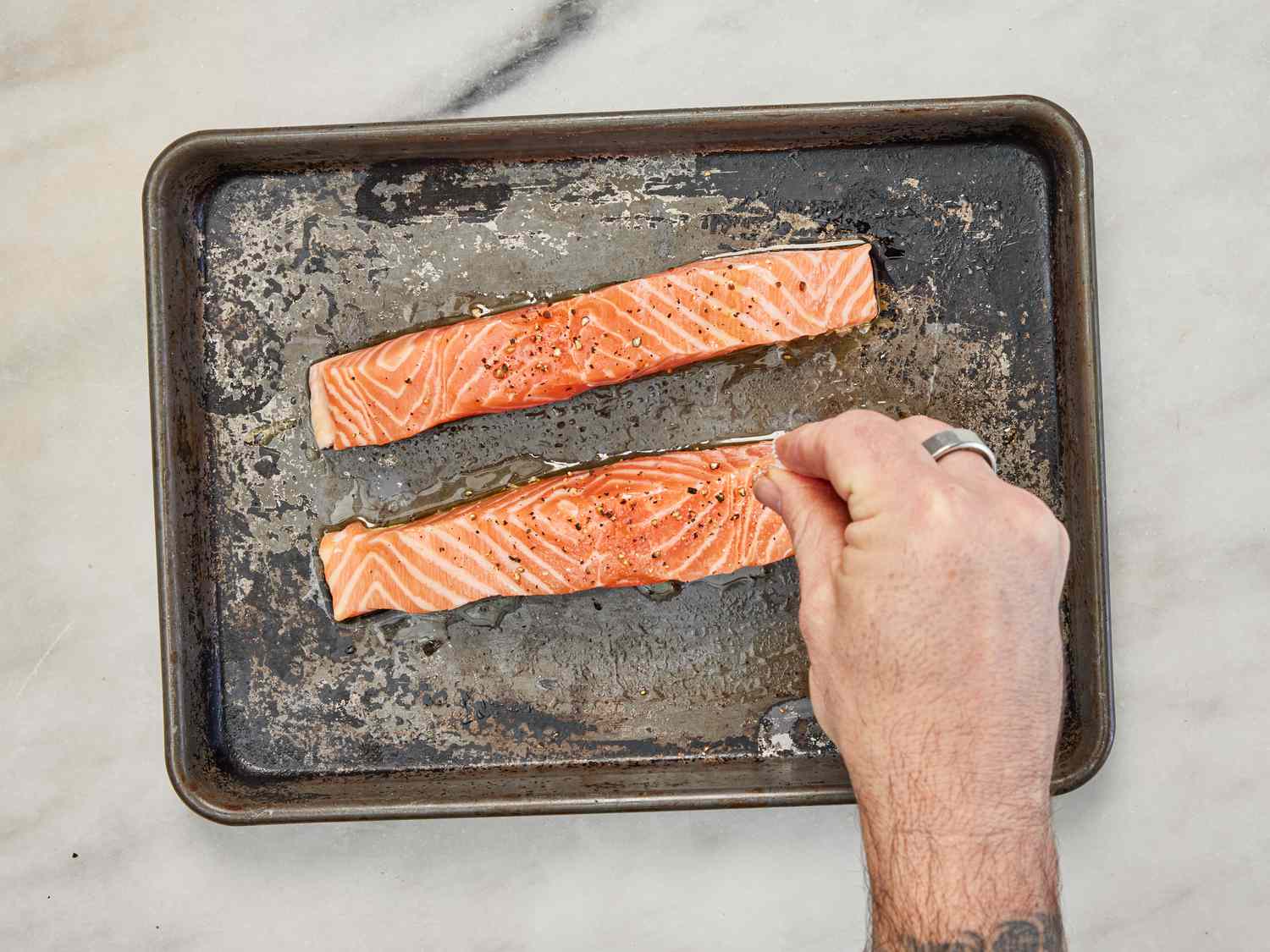Slices of salmon fillet are seasoned on a quarter-size baking sheet.