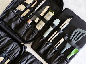 A black carrying case containing various kitchen tools including knives a grater tongs and spatulas organized in pockets