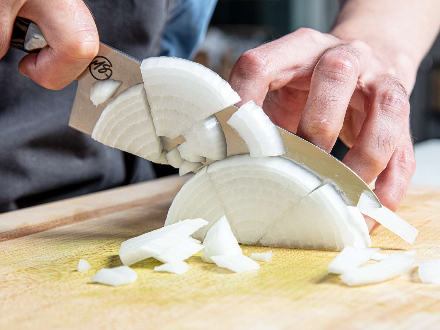 Half an onion cut in thirds being sliced on a wood cutting board