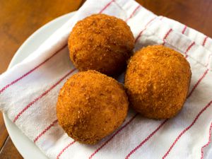 Several golden brown arancini lying on a plate lined with a patterned kitchen towel.