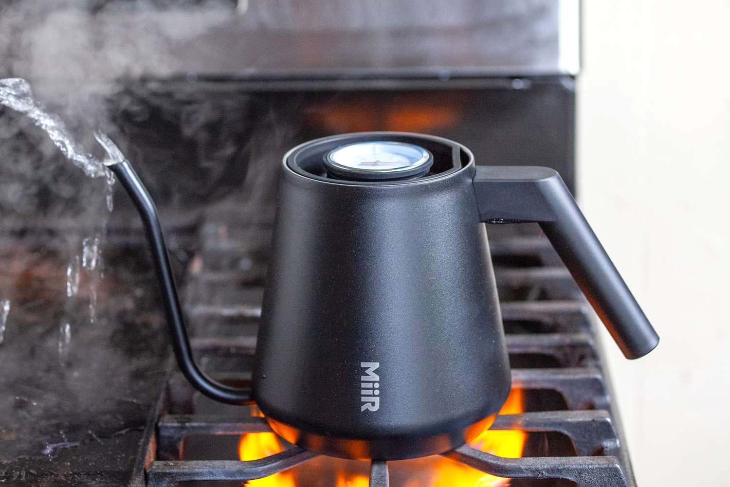 A kettle on a stovetop emitting steam from the spout