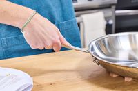 A person holds the handle of the All-Clad D3 Stainless-Steel 12-Inch Fry Pan