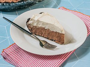 A slice of pie with whipped topping served on a plate with a fork on a striped napkin