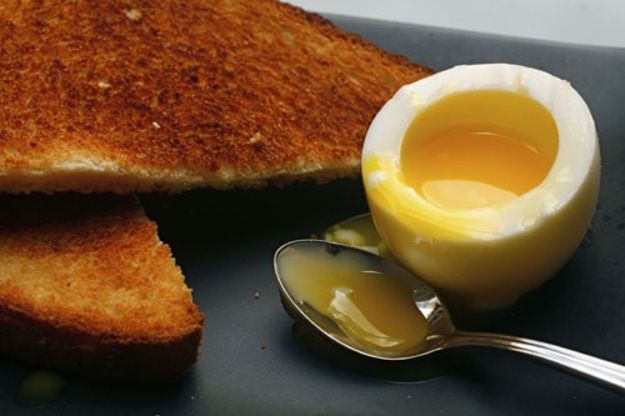 A soft-boiled egg, with the top removed to reveal runny yolk inside, served with toast.