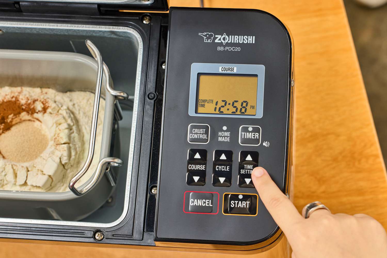 A finger pressing a button on an opened Zojirushi Home Bakery Virtuoso Plus Bread Maker