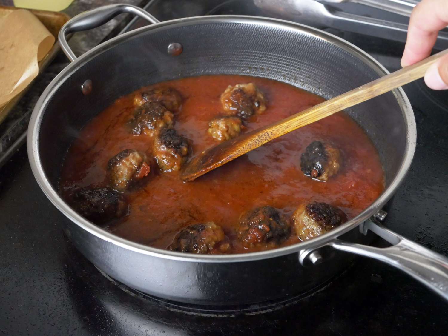 a person stirring tomato sauce with meatballs in a saute pan