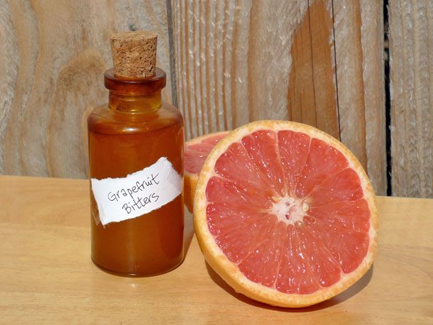 A small corked bottle of grapefruit bitters is set next to a halved pink grapefruit.