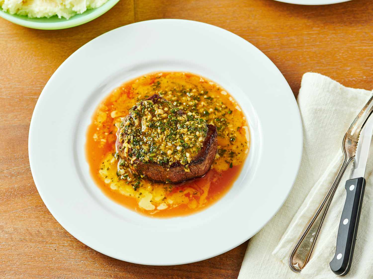 Plated steak with herbed sauce and utensils on a napkin nearby