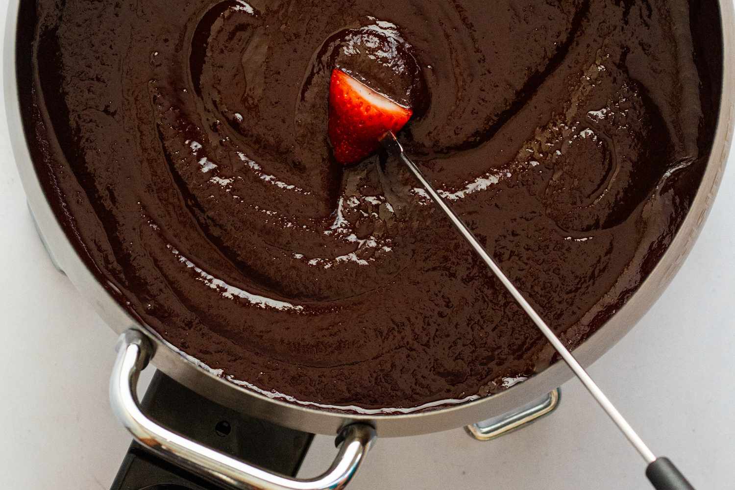A fondue fork dragging a strawberry through chocolate fondue.
