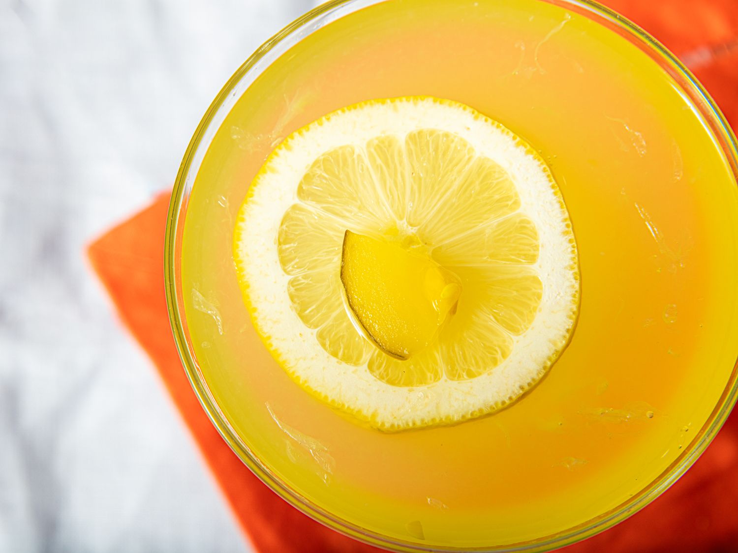 A mezcal pickle lemonade garnished with a slice of lemon and pickle piece top view