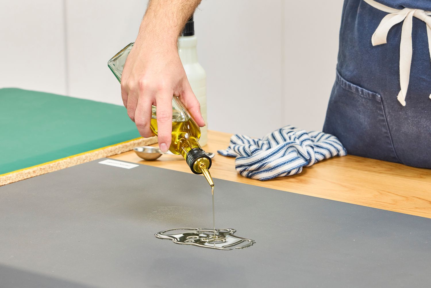 A person pours oil onto the WellnessMats Original Anti-Fatigue Floor Mat