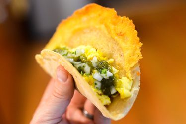 Hand holding a taco overflowing with crispy manchego cheese 