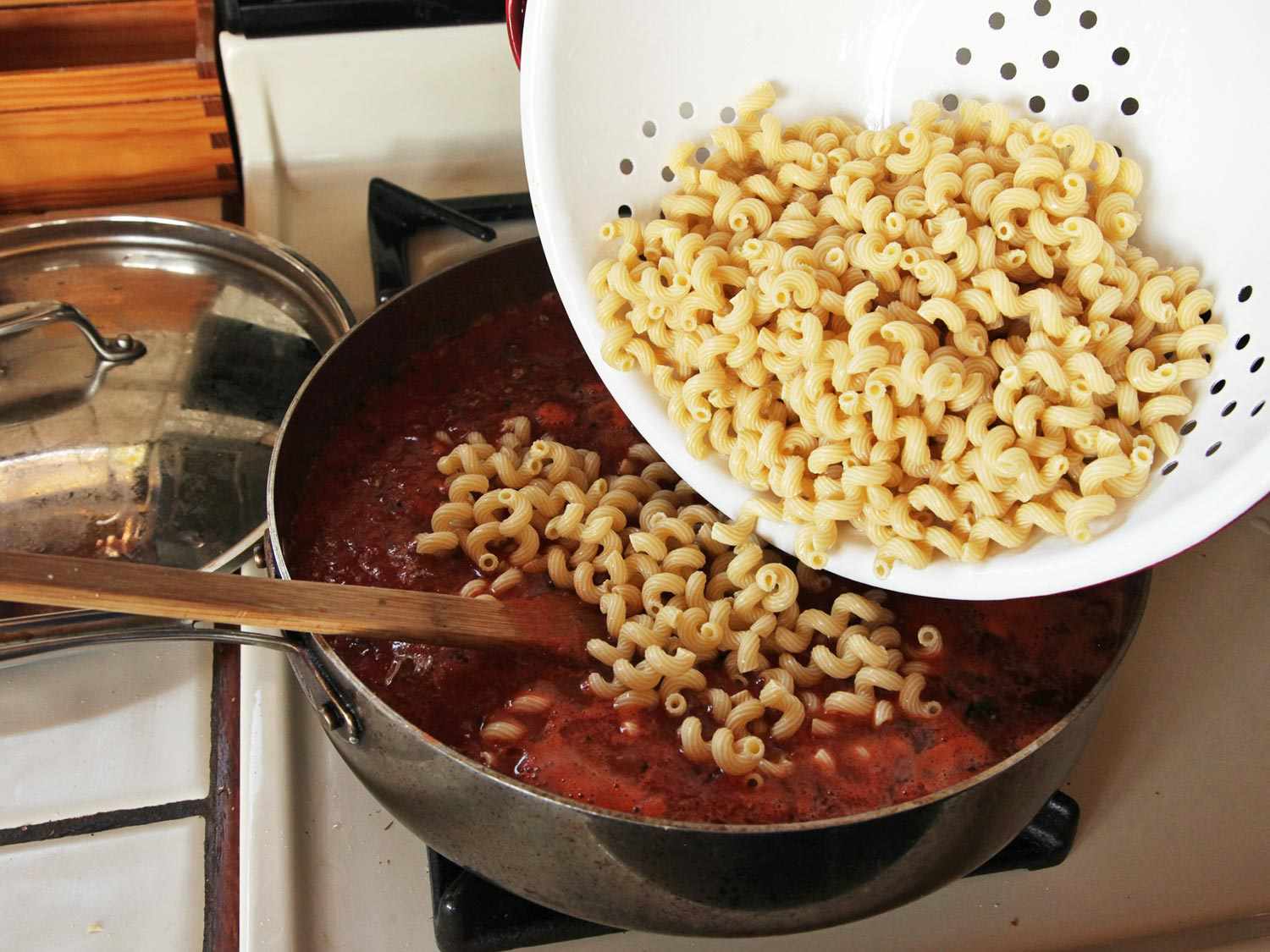 The pasta is being added to the pan from the colander. 