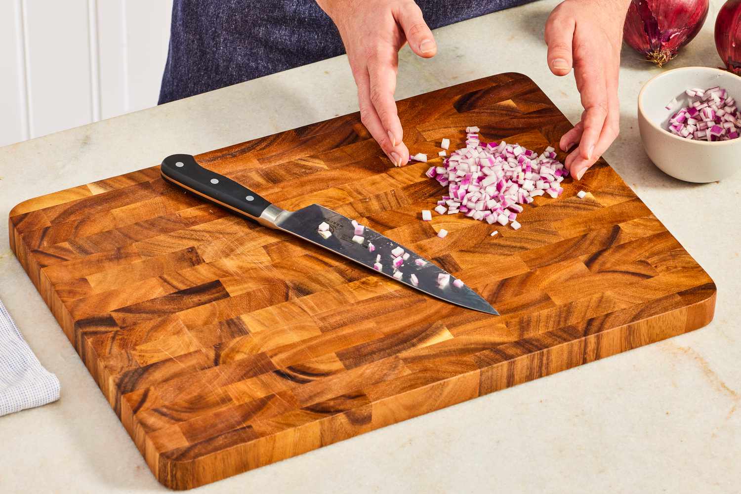 A person chopping red onion on a wooden cutting board