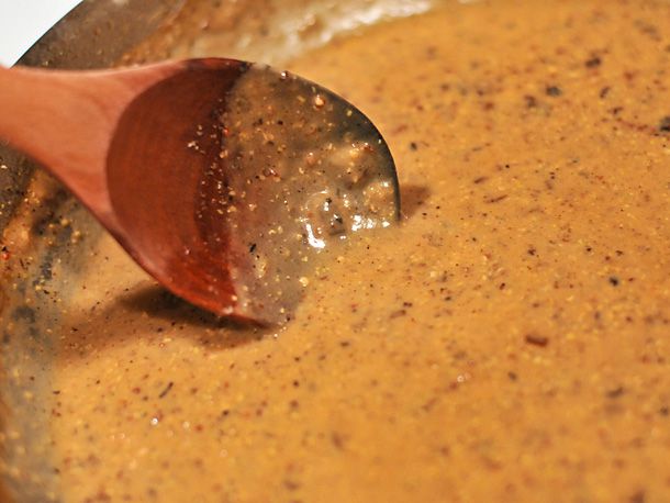 Stirring thickened mustard sauce in a skillet with a wooden spoon.