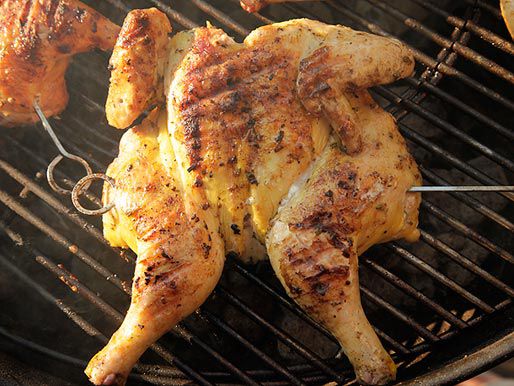 Close-up of a butterflied chicken on the grill, its skin looking a little mangled and unevenly charred.