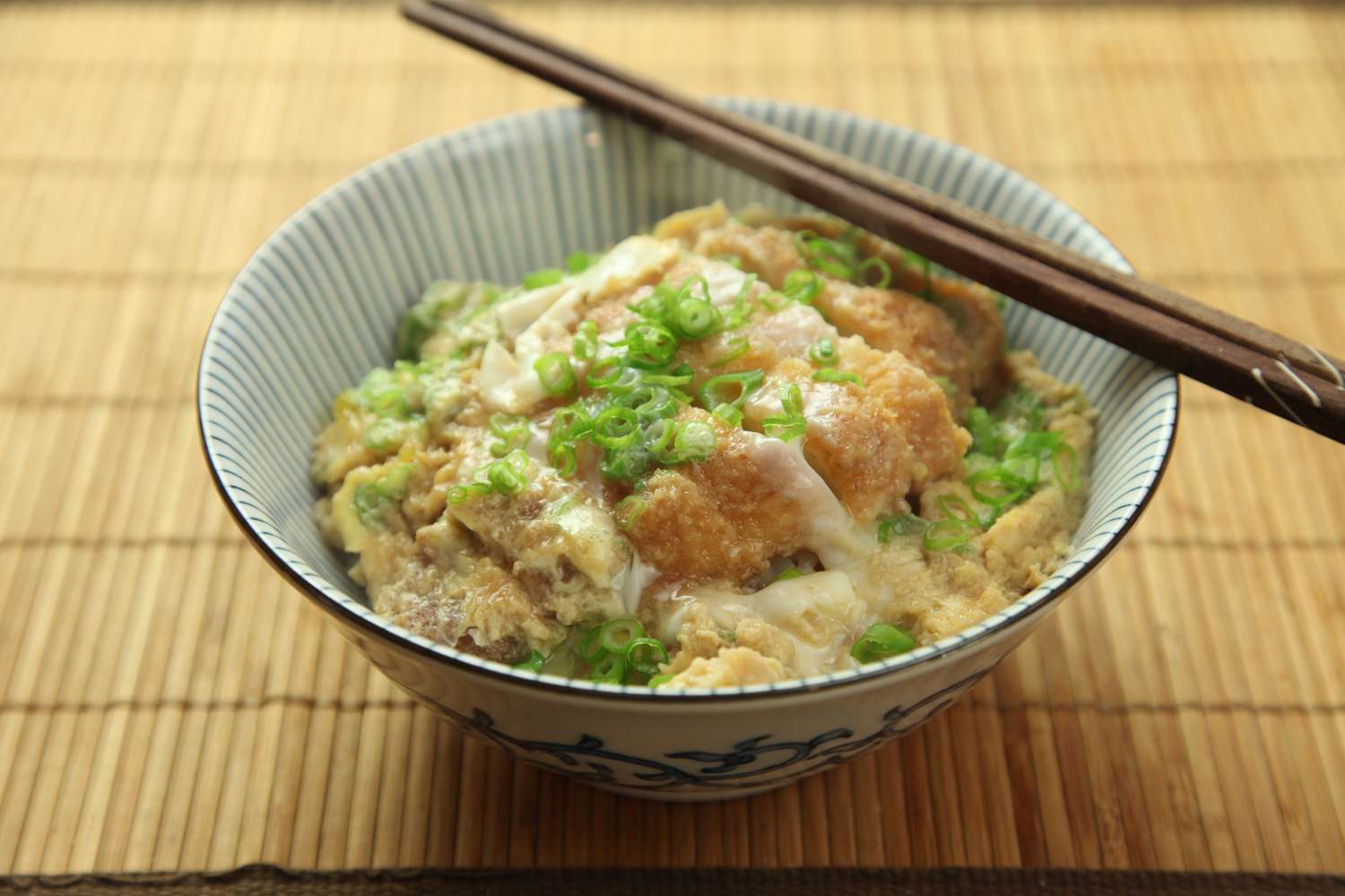Katsudon resting in a bowl with chopsticks on the rim 