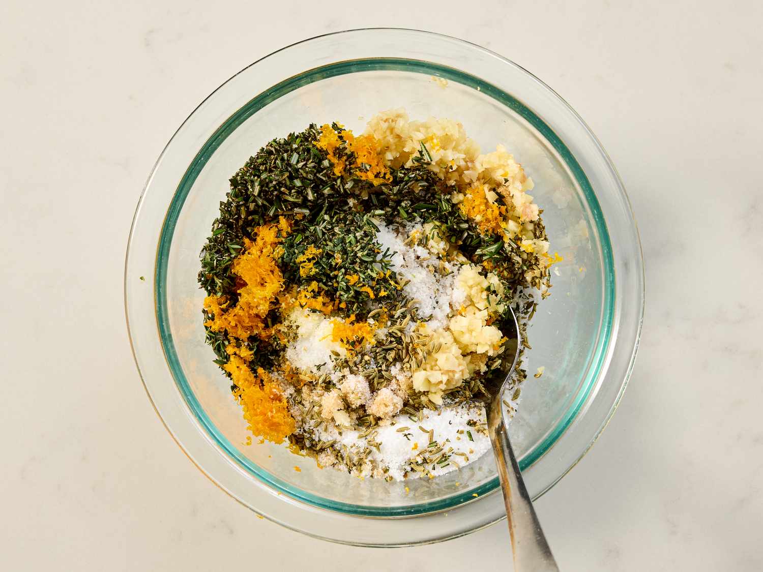 A bowl containing a mixture of herbs spices and other seasoning ingredients with a spoon
