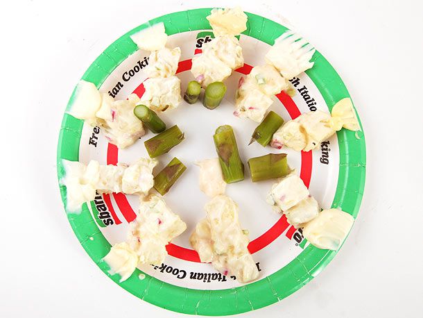 Paper plate covered in various mayonnaise samples for a taste test along with sections of asparagus spears for tasting.