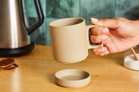 A person picking up a tan ceramic mug.