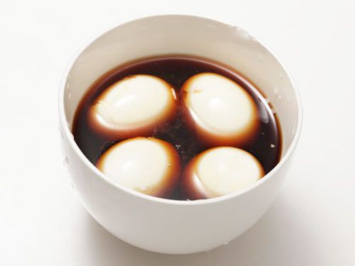 Four soft-boiled eggs marinating in a soy sauce mixture in a white bowl.