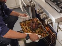 a person putting a full roasting pan into the oven