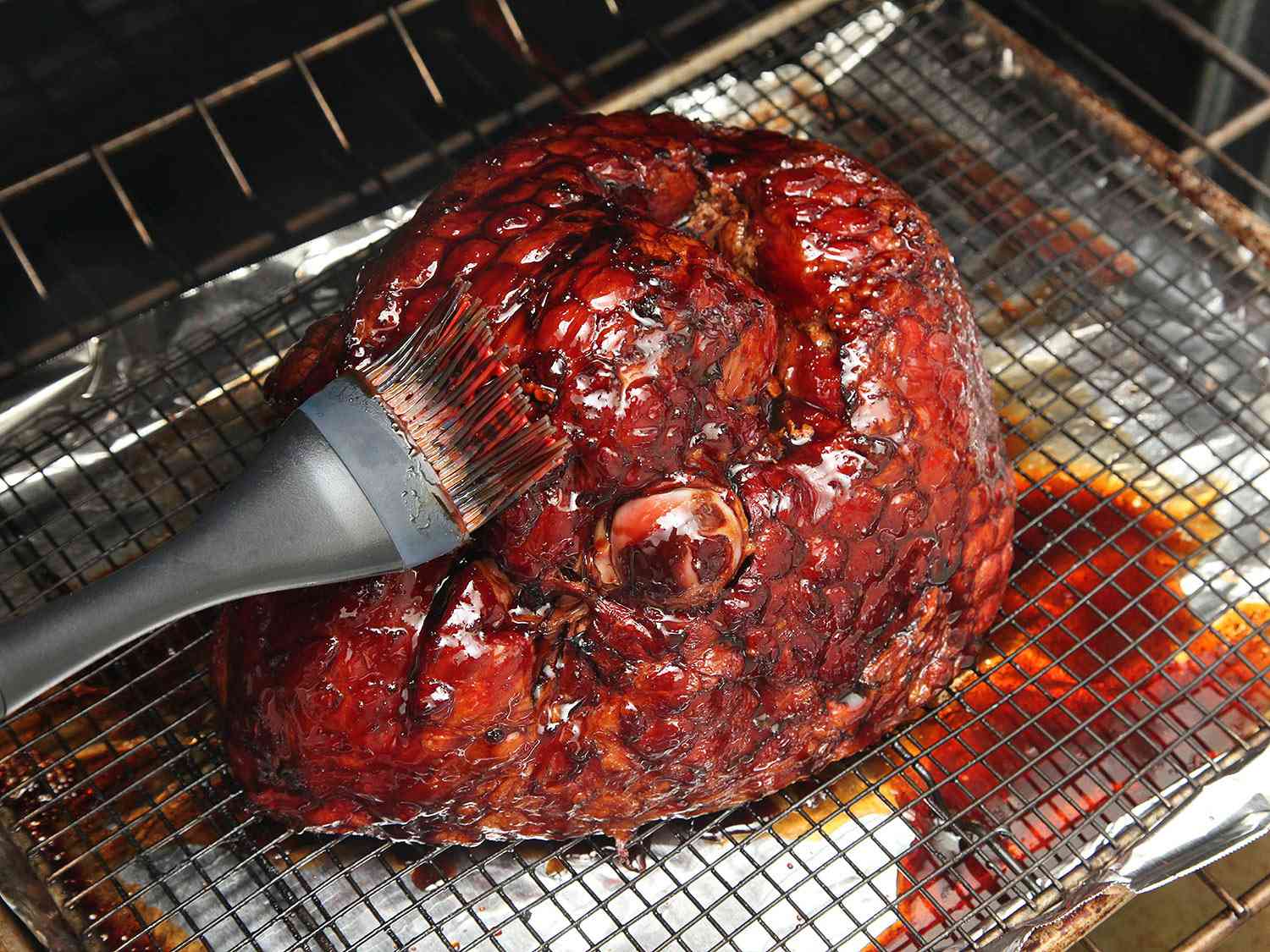Brushing glaze onto ham on a wire rack set over a rimmed baking sheet. 