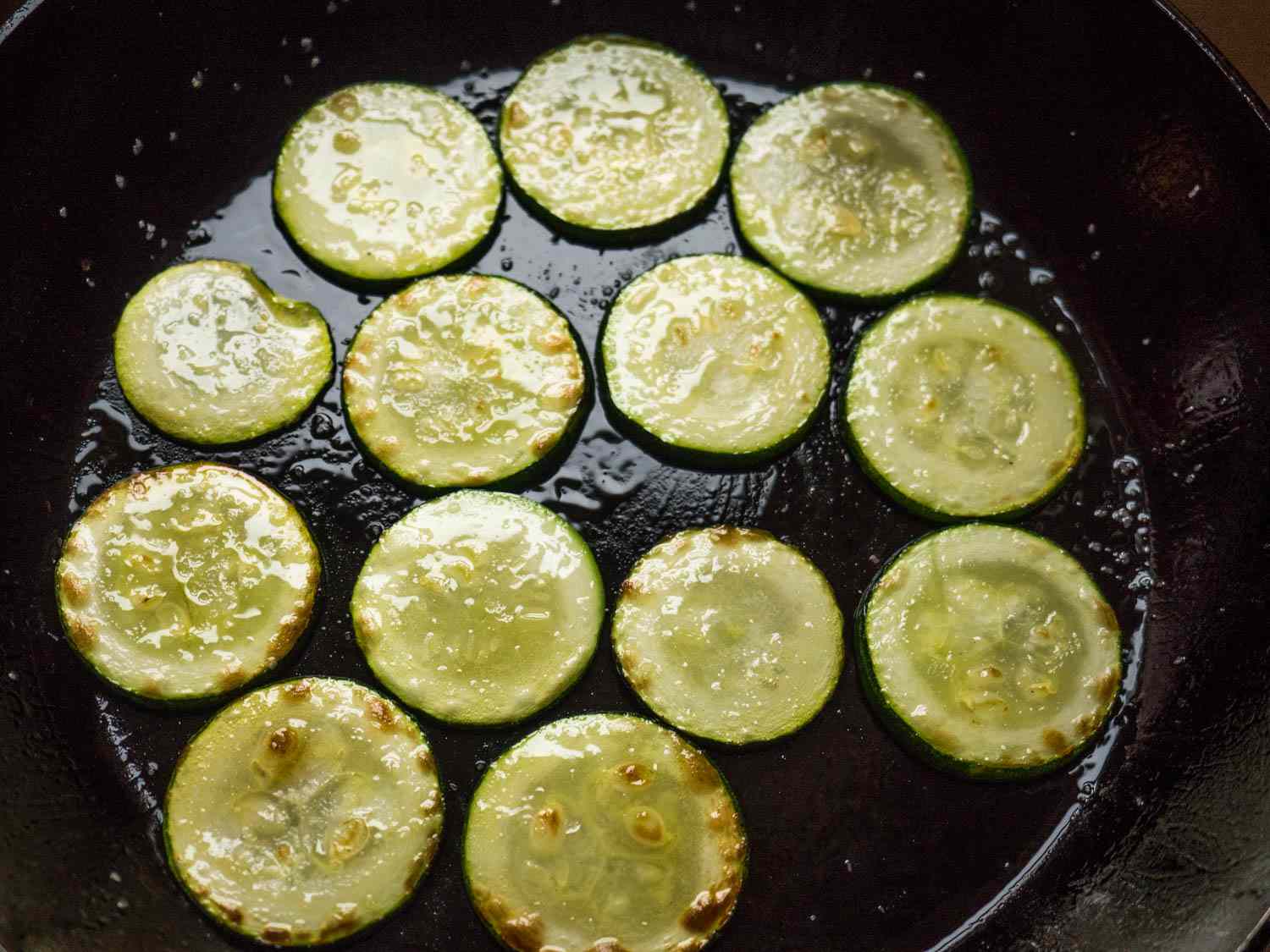Overhead shot of zucchini slices being browned in a skillet.