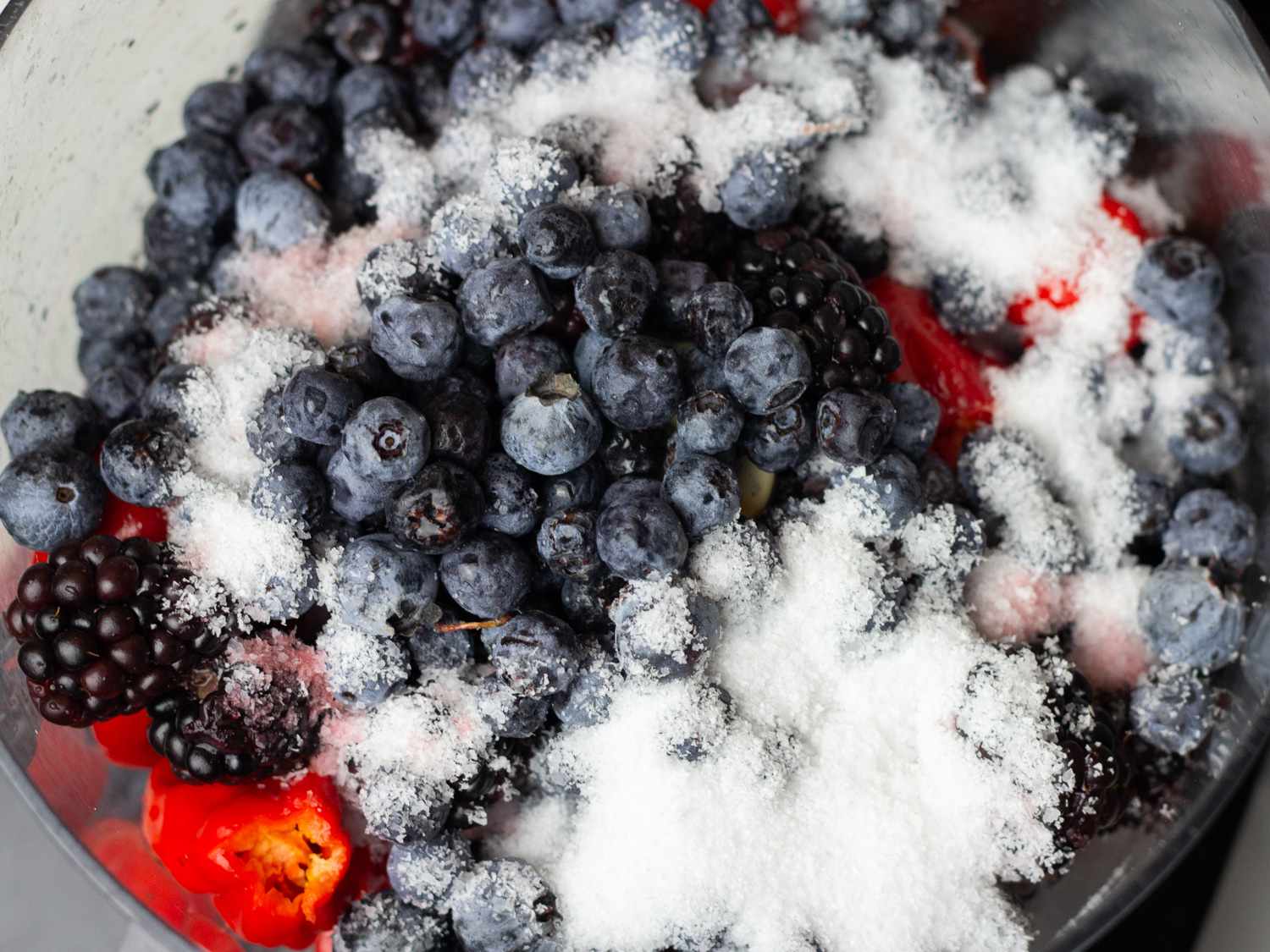 Adding salt to a mash of berries and chile peppers for hot sauce.