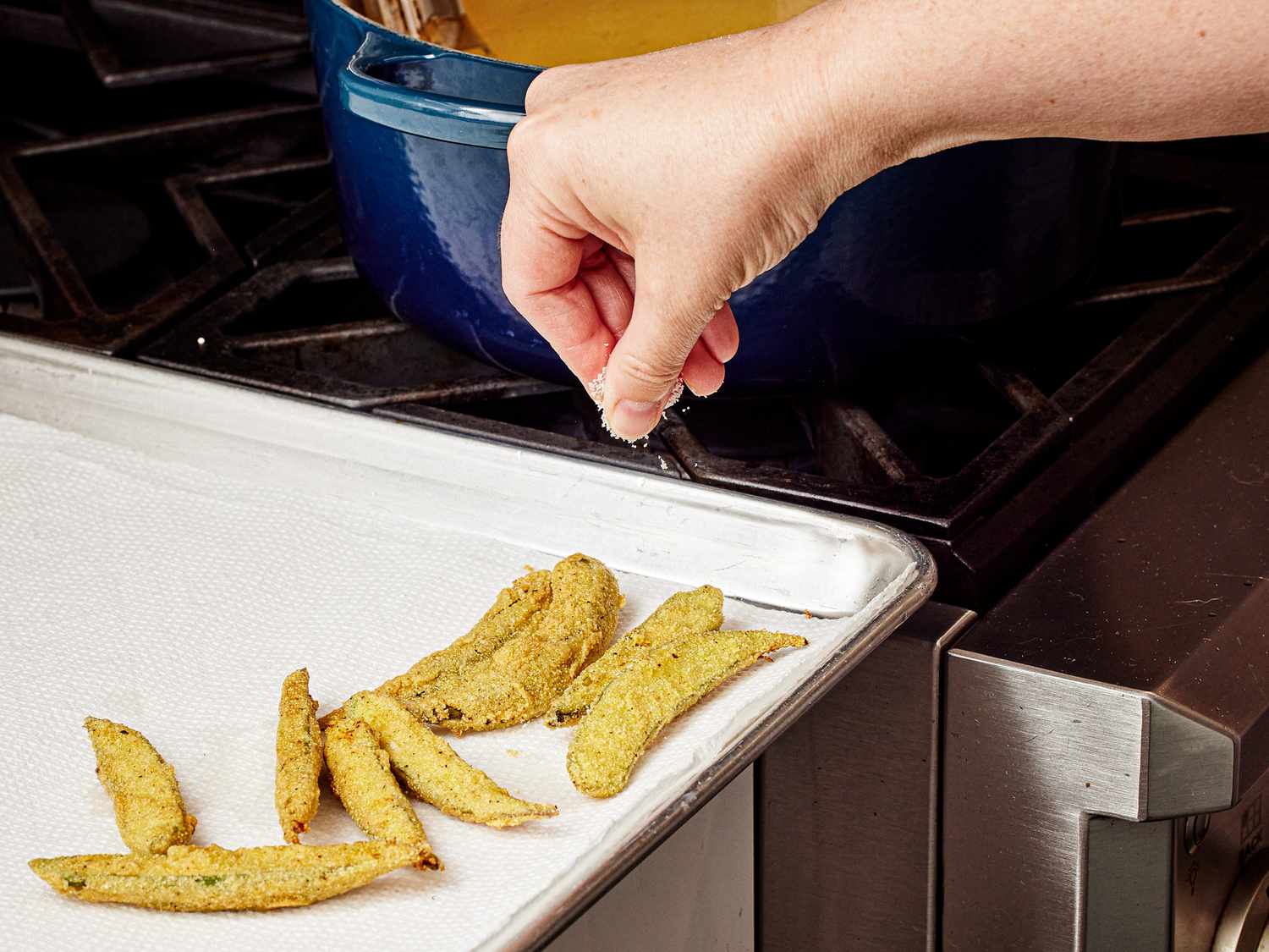 Salting fried okra thats on a paper towel lined sheepan