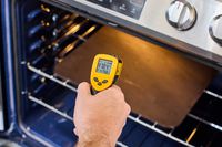 A person taking the temperature of a pizza steel in the oven with an infrared thermometer.