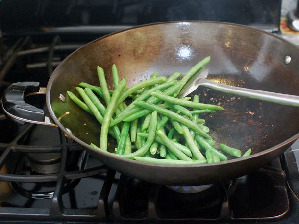Stir-frying blanched green beans in a hot wok with oil