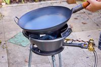 A person placing a wok onto an outdoor wok burner.