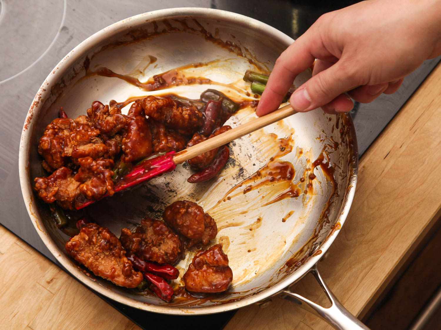Tossing fried chicken thighs in sauce for General Tso's chicken.