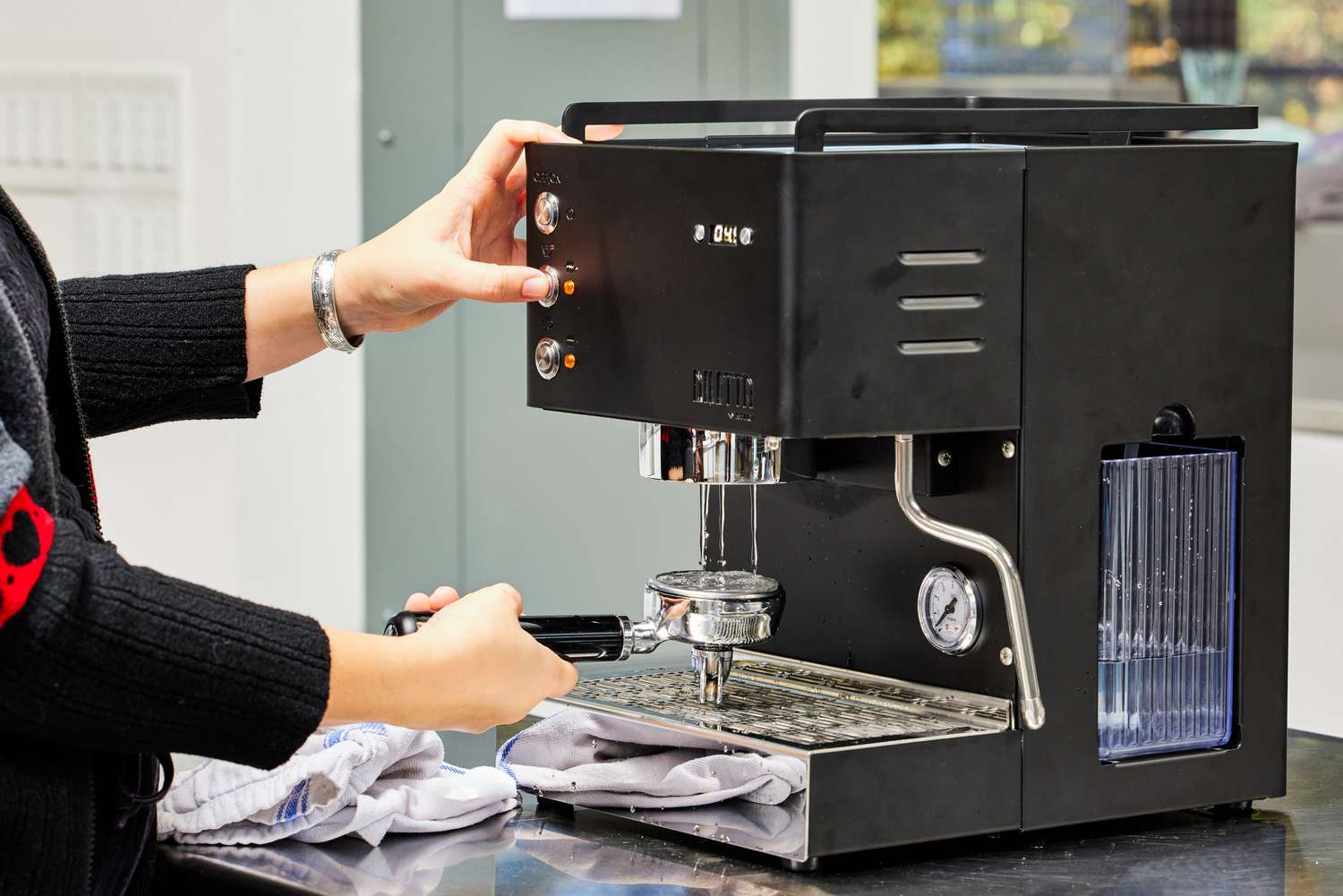 A person pressing one of the buttons on the Diletta Mio Espresso Machine and holding the portafilter 