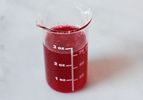 A 3 oz beaker filled with vivid red cranberry syrup.