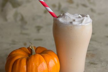 Pumpkin bourbon cider milkshake, served in a pint glass next to a miniature pumpkin.