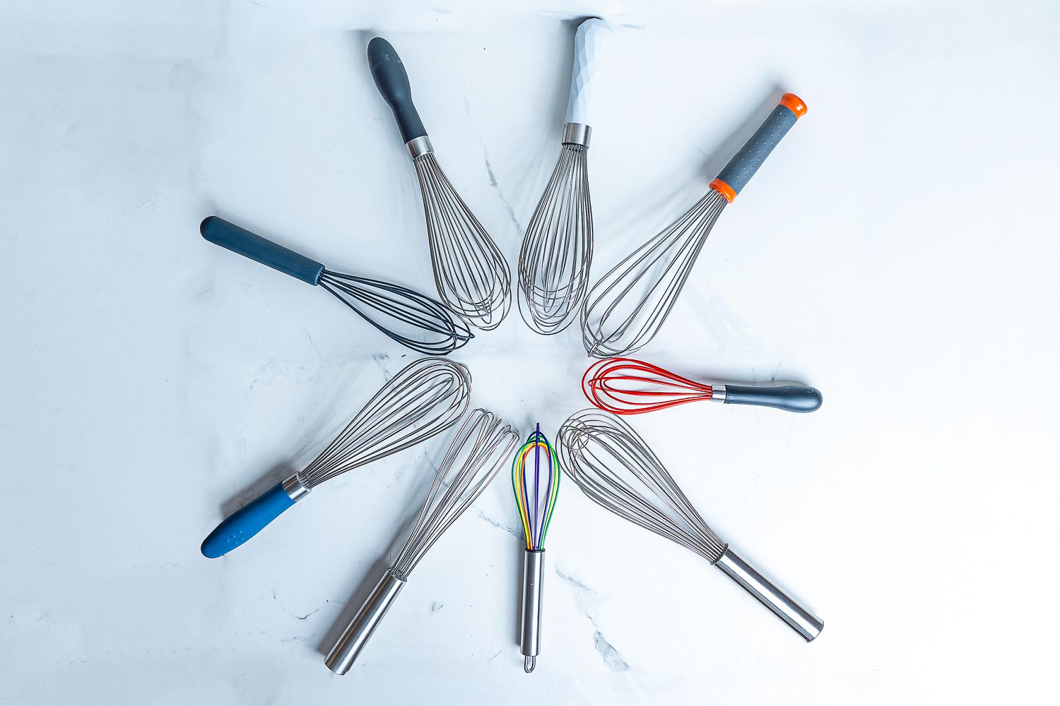 Nine whisks arranged in a circle on a white marble countertop