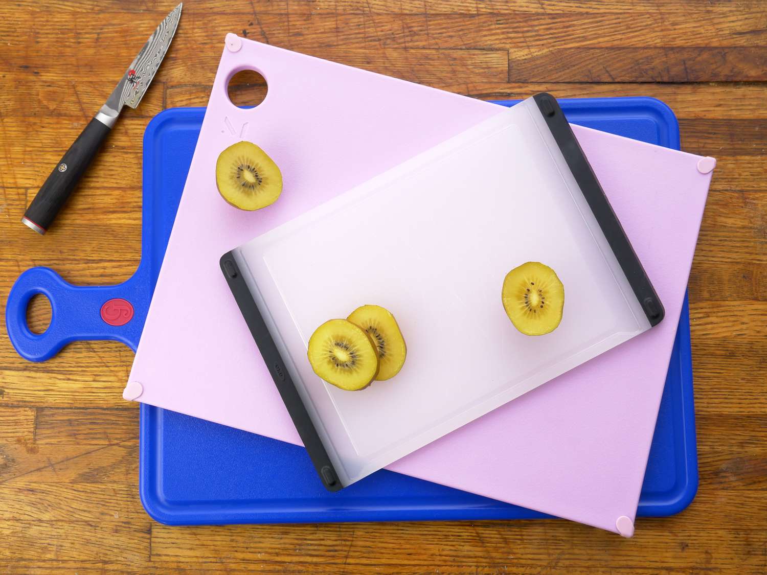 three plastic cutting boards with sliced kiwi and a paring knife