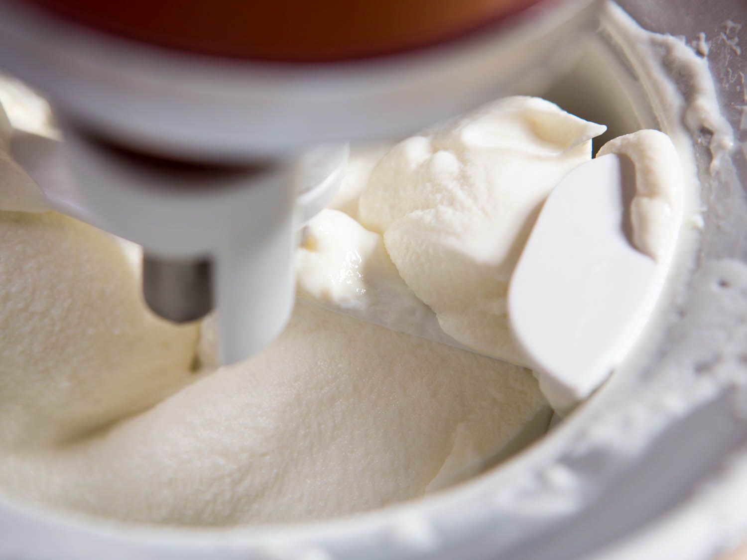 Close-up shot of soft-serve vanilla bean ice cream being mixed inside a freezing core attached to a mixer. 