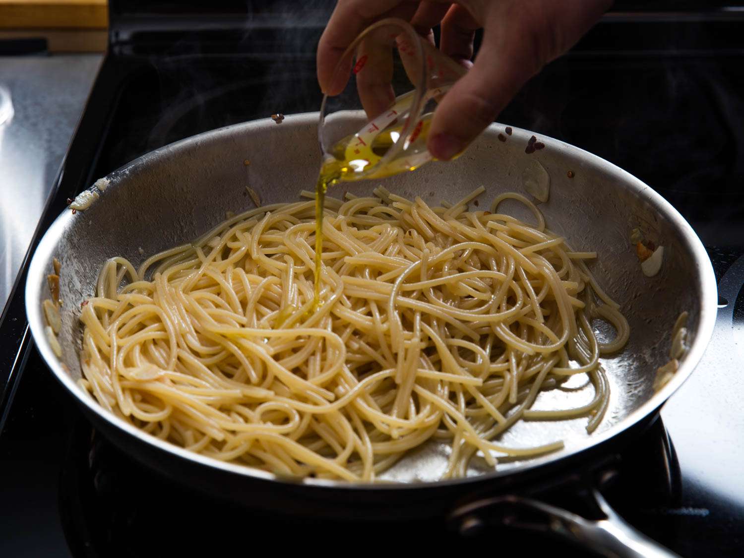 drizzling fresh olive oil over aglio e olio pasta in skillet