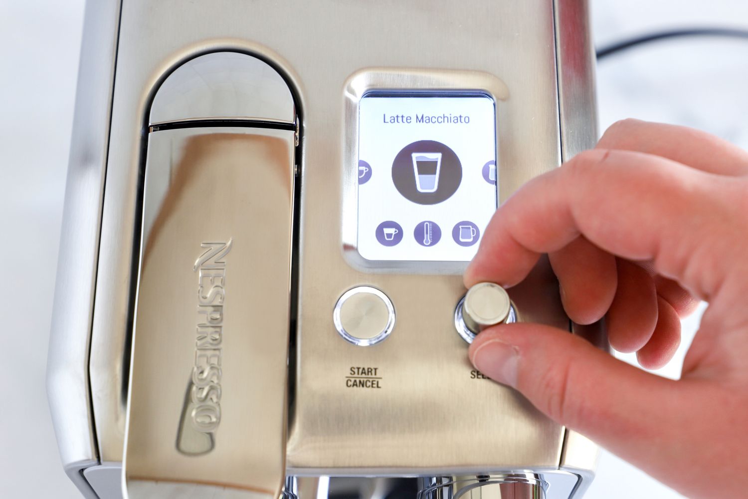 A persons hand adjusting a knob on a Nespresso machine with a display showing a latte macchiato option