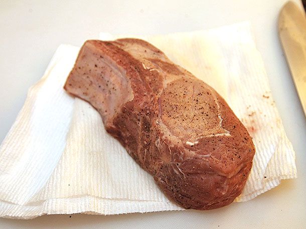 Sous vide double-cut pork chop being patted dry on a paper towel. 
