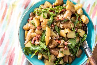 A bowl of fingerling potato salad with chorizo, onion, and arugula. 