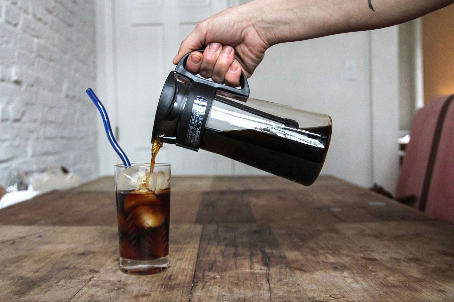 A person pouring cold brew from a carafe into a glass.