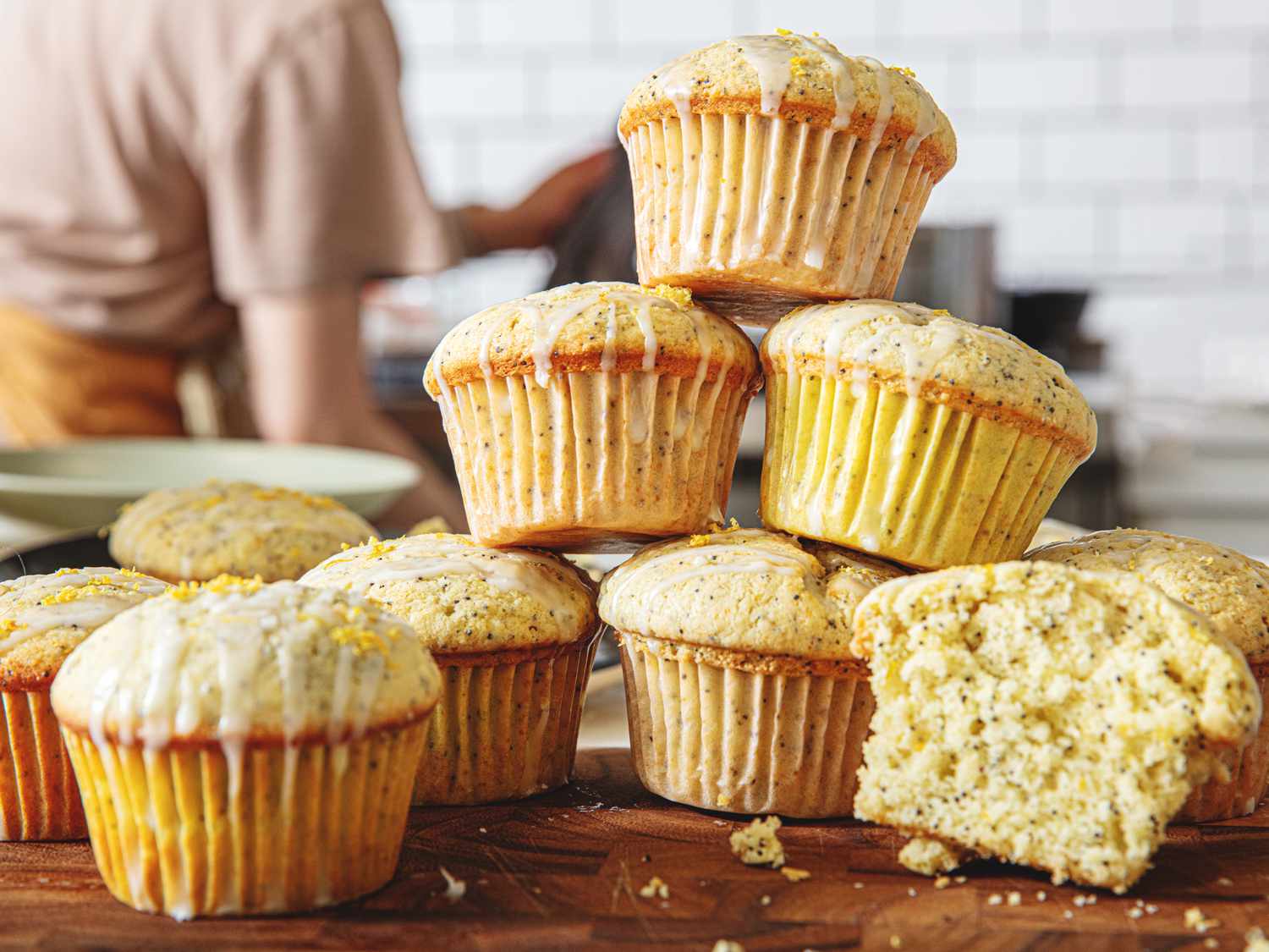 Lemon poppy seed muffins stacked on a wooden surface, with a partially sliced muffin showing the interior